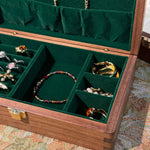 Jewelry box with green interior displaying various jewelry items on a patterned fabric background.